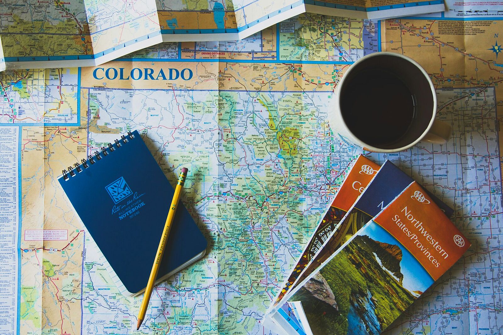 Une carte routière dépliée sur une table, avec un carnet, un crayon, des brochures de voyage et une tasse de café.